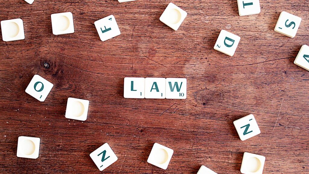 Scrabble tiles spelling 'LAW' on a wooden table, symbolizing connections to education and legality.